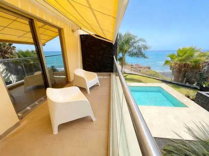 Bedroom balcony with awning, glass railing and a view over the pool to the sea