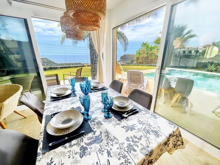 Dining table set for six by sliding doors open to the garden, pool and sea