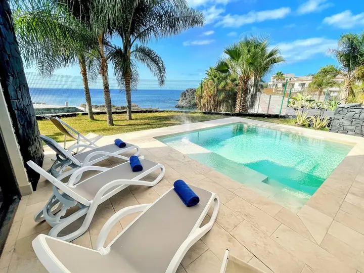Sun loungers with Villa de Nava towels beside the private pool, palm trees and the ocean behind