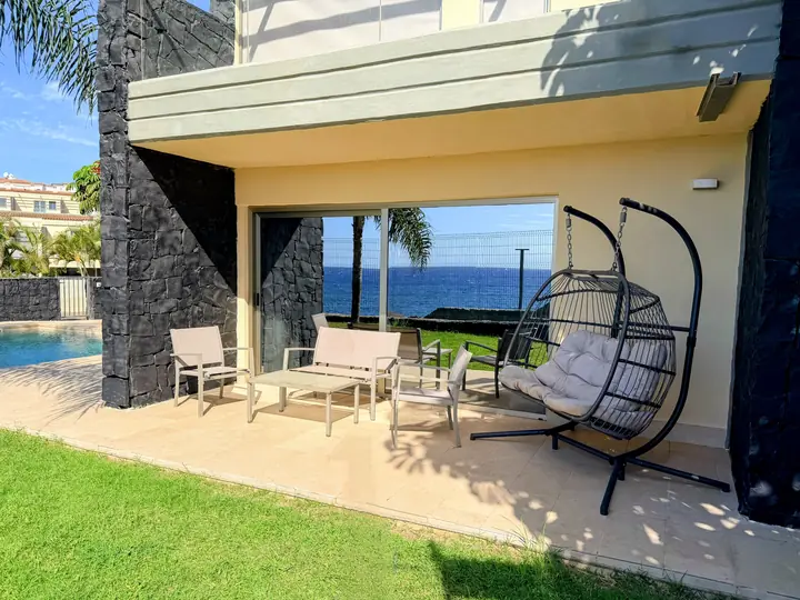 Covered terrace with sofa set and hanging egg chair, the sea seen through the glass